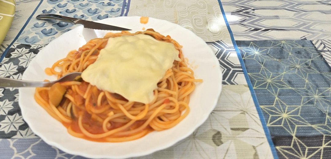 흰 접시에 담긴 토마토 소스 스파게티 위에 녹인 치즈 한 장이 얹혀 있다