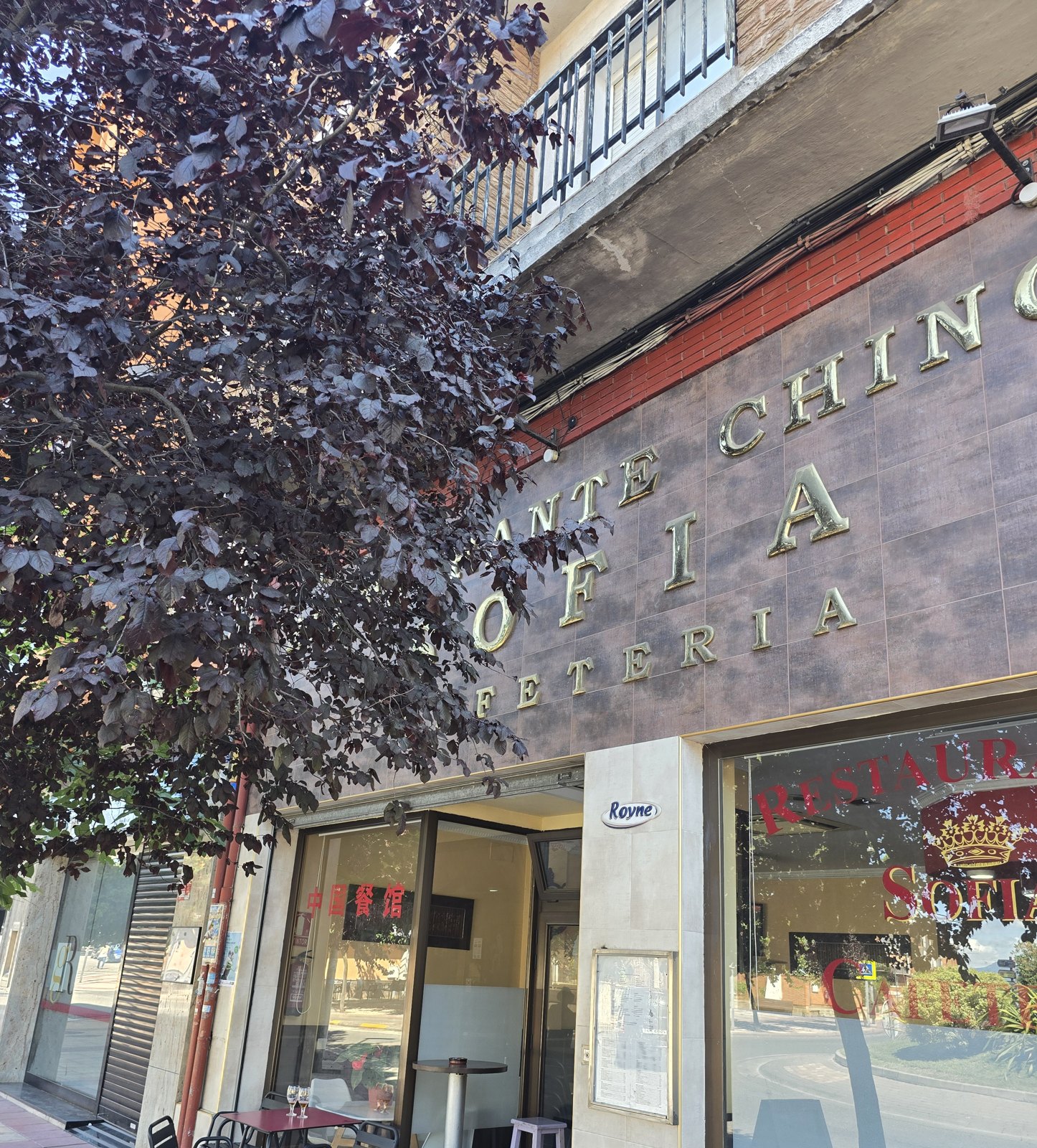 건물 벽에 금색 글자로 RESTAURANTE CHINO SOFIA CAFETERIA라고 붙어 있다. 아래 유리문 안쪽에 붉은 바탕의 중국어 간판이 걸려 있고 인도에 탁자와 의자가 놓여 있다