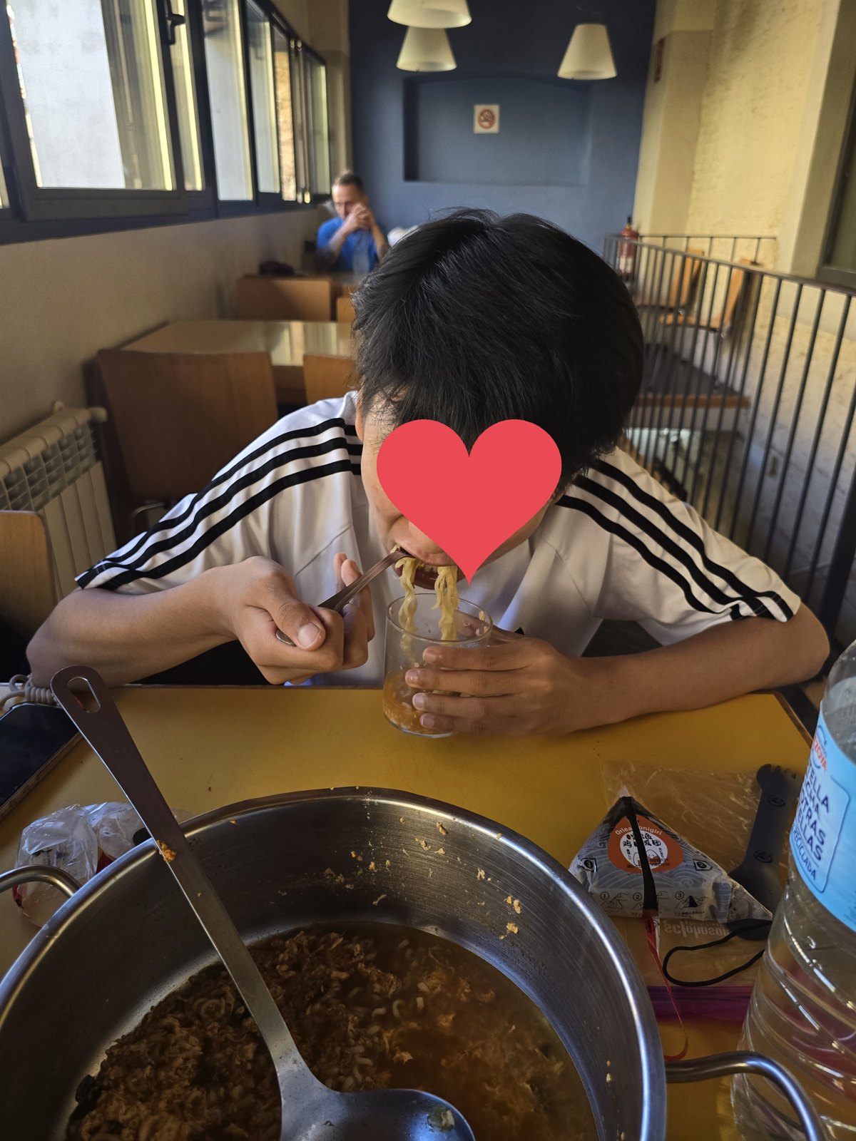 알베르게 식당의 노란 탁자 위에 라면을 끓인 큰 냄비와 국자가 놓여 있고, 유리컵에 덜어 낸 면을 젓가락으로 먹고 있다. 옆에 삼각김밥 포장이 있다