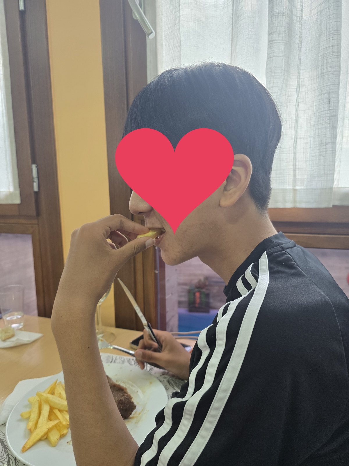 식당 식탁에 감자튀김과 고기가 담긴 접시가 놓여 있고 한 사람이 앉아 포크로 감자를 집어 먹고 있다