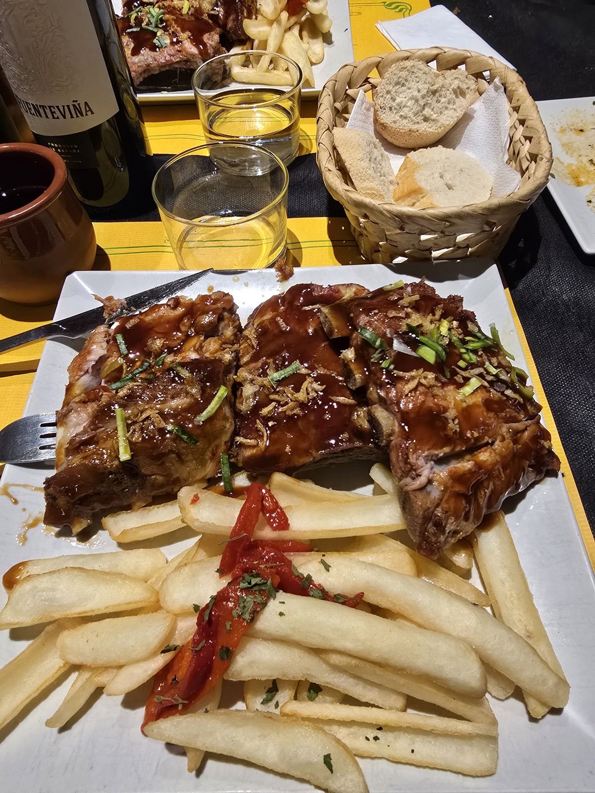 긴 접시에 양념한 갈비 여러 대와 흰 아스파라거스가 담겨 있고 옆에 빵과 와인잔이 놓여 있다