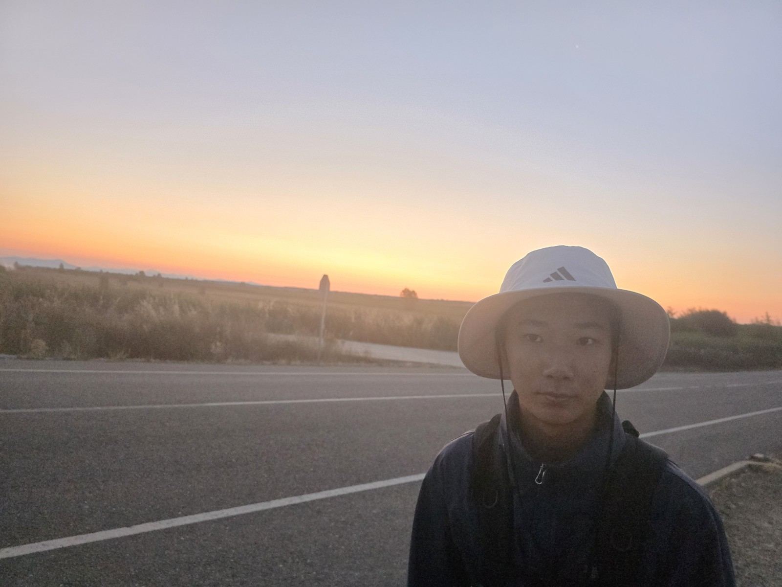 지평선 위로 해가 떠오르며 하늘이 주황빛으로 물든다. 도로가 그 방향으로 곧게 뻗어 있다