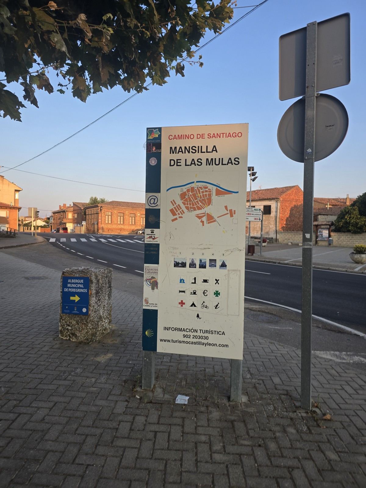 파란 안내판에 MANSILLA DE LAS MULAS 지도가 그려져 있다. 뒤로 성벽이 보인다