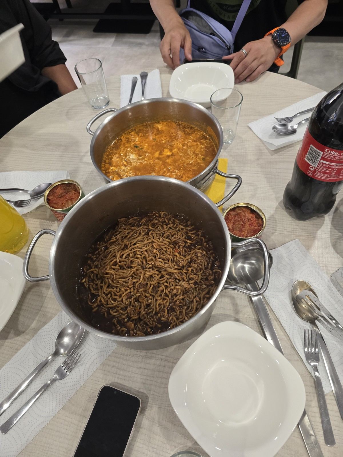 스테인리스 냄비에 담긴 볶음면과 국물 요리가 흰 접시들과 함께 상 위에 차려져 있다