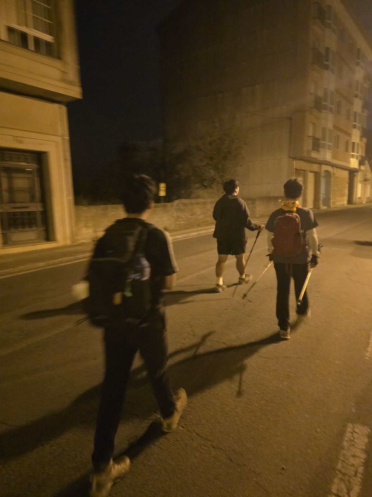 가로등 켜진 새벽 도로를 배낭 멘 순례자 셋이 뒷모습으로 걸어간다