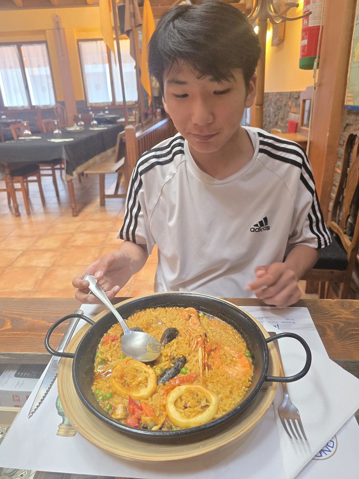 검은 팬에 담긴 노란 쌀 요리. 새우와 홍합, 채소가 섞여 있다