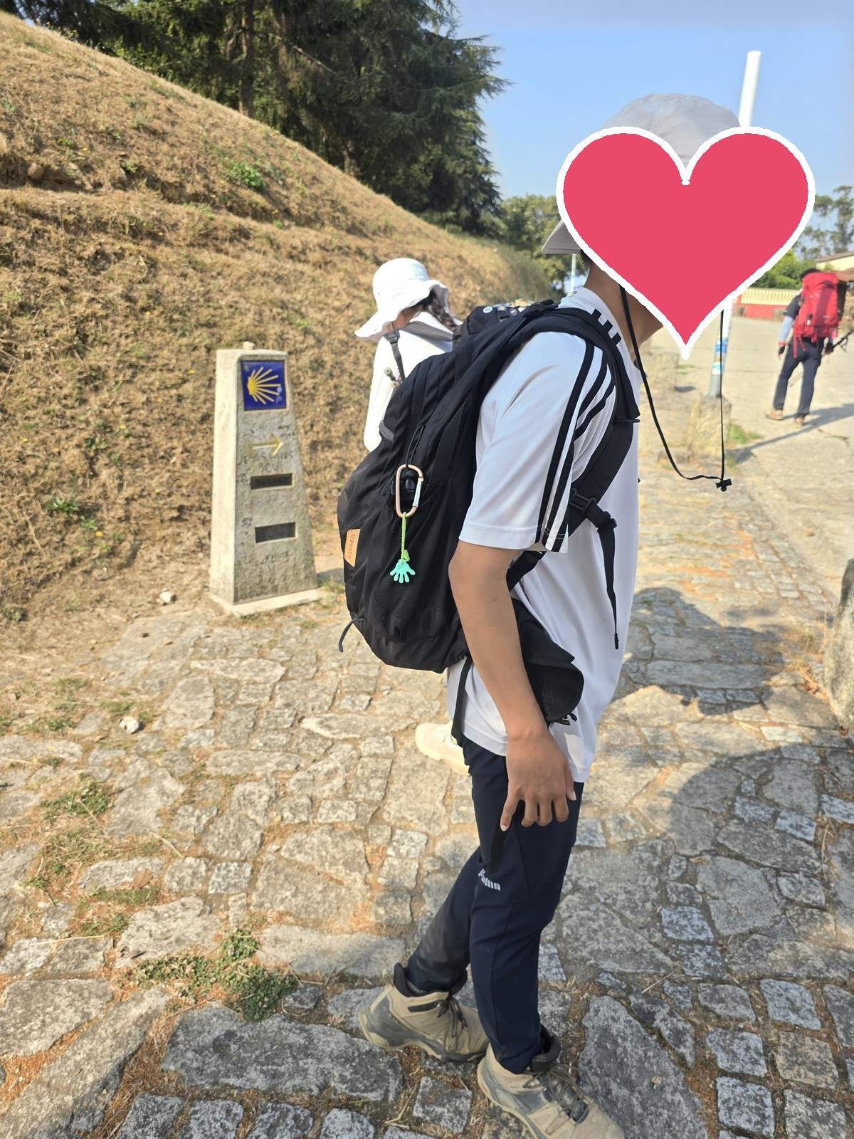 배낭 멘 순례자가 조가비 표식이 붙은 화강암 이정표 옆 돌길에 서 있다