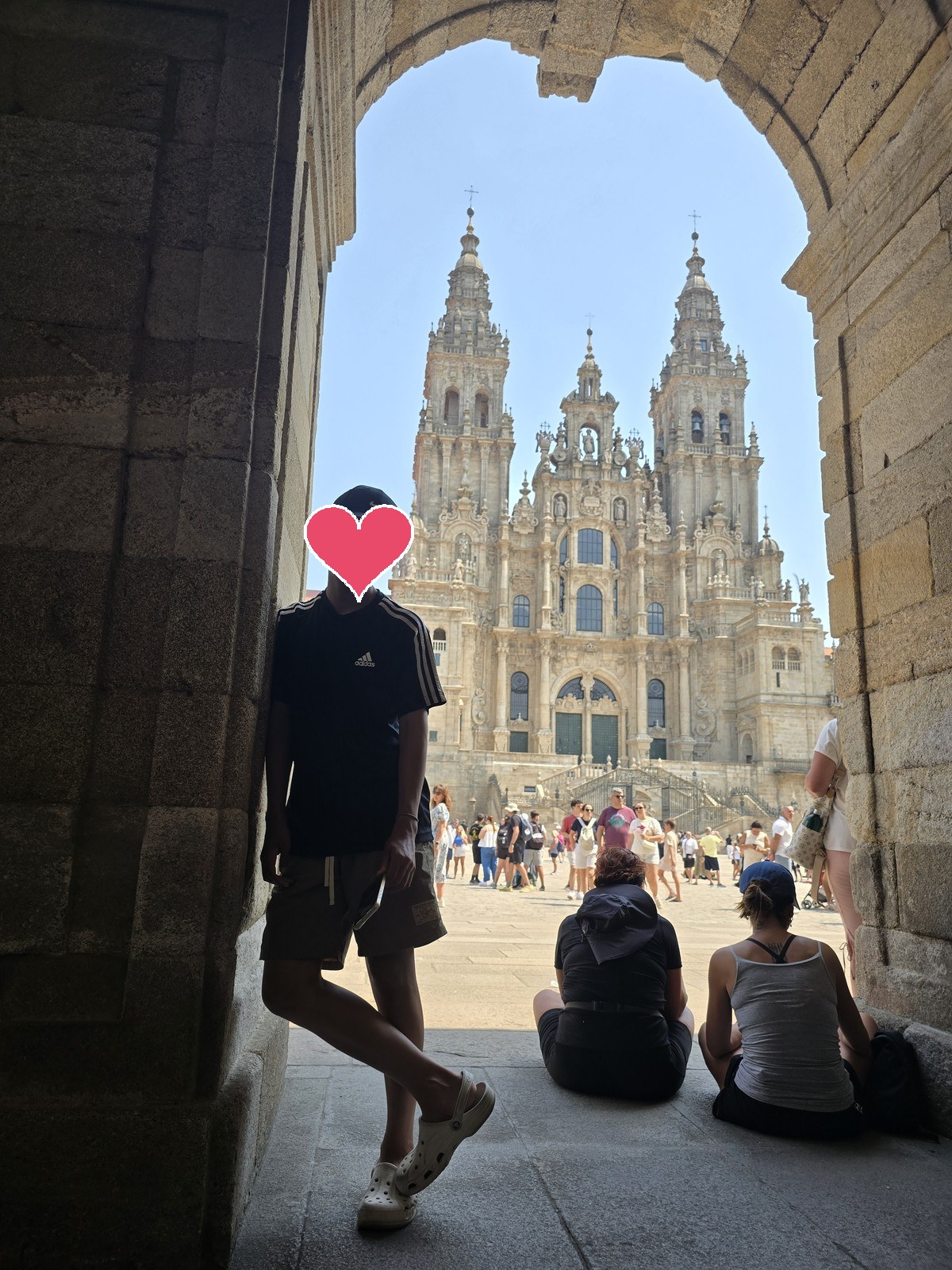 돌 아치 아래 그늘에 선 사람 너머로 오브라도이로 광장과 대성당 정면이 보인다