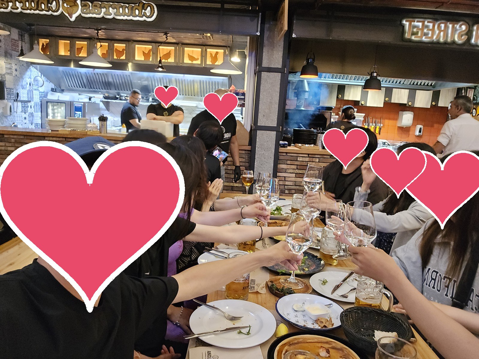 시장 안 식당의 긴 나무 식탁에서 여러 사람이 잔을 들어 건배하고 있다